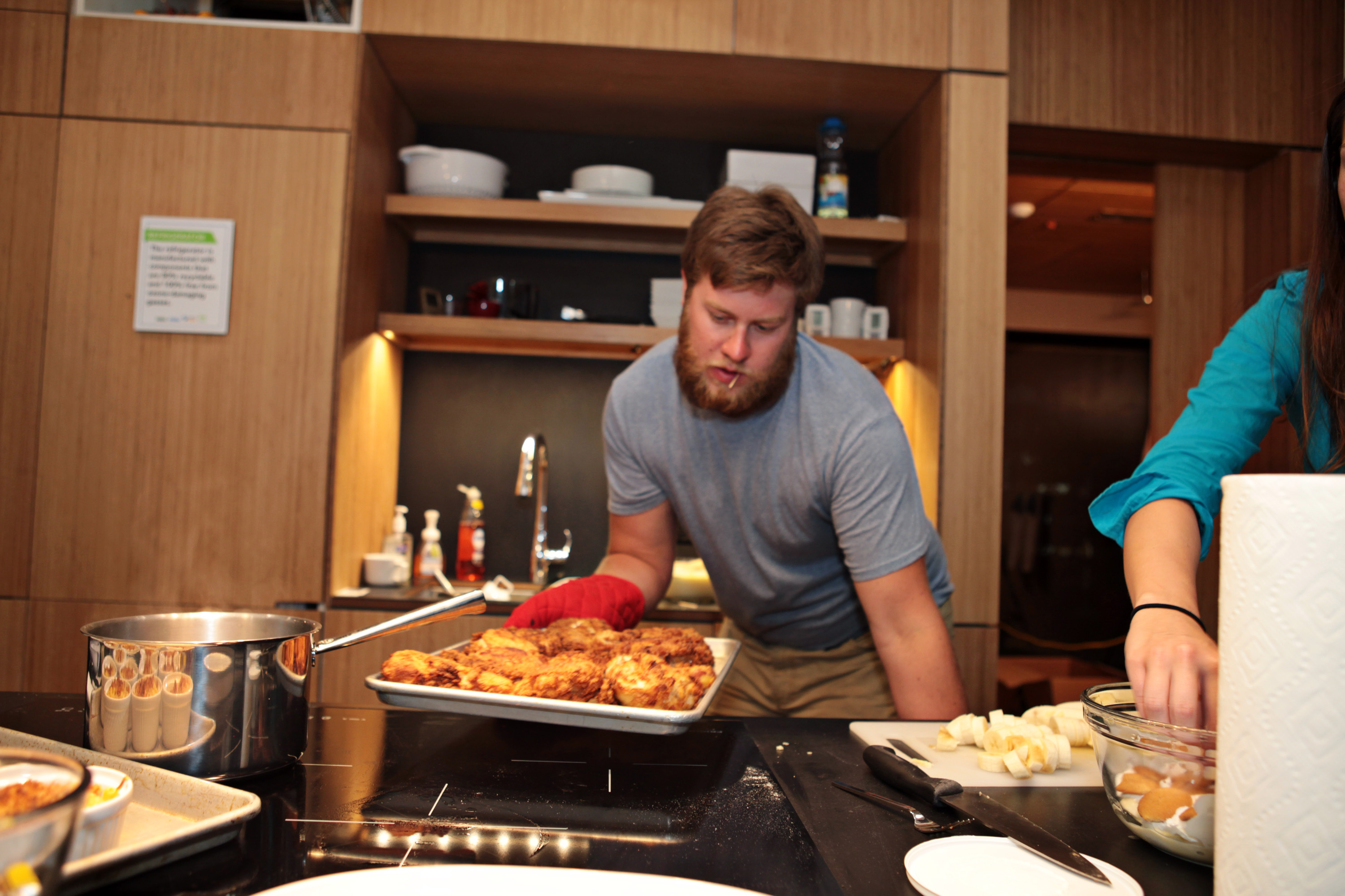 Photo of a young man wearing an oven mitt and holding a pan of food above a stove.