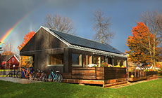 Photo of Self-Reliance surrounded by trees, grass, and bicycles. A rainbow is visible in the sky.