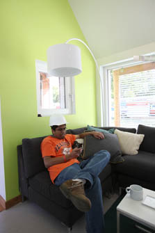 Photo of a man sitting on a couch in the living room of the Illinois house and looking at his cell phone.